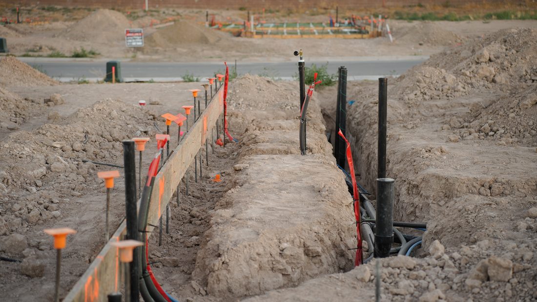 Open utility trenches with conduit and survey stakes on a residential development