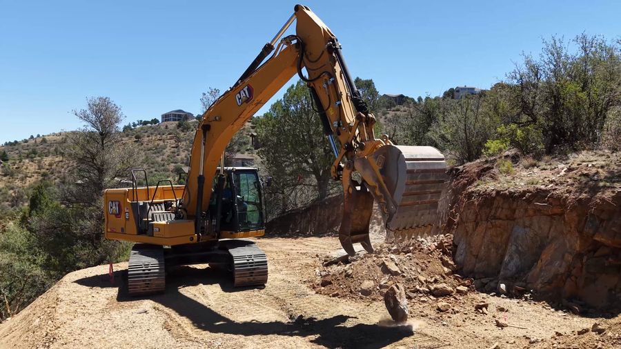 CAT excavator digging into a rock cut on a rural Yavapai County property